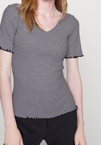 Black and white striped short-sleeve top with a V-neck and frilled edges. Soft fabric with a fitted silhouette.