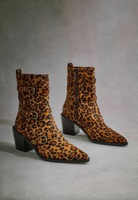 Anatomske cipele s uzorkom leoparda, s izduženim prstima, smešanim smešnim i crnim nijansama, teksturom sličnom krznu i srebrnim kopčama na trakama, s srednje visokim blok-petama.