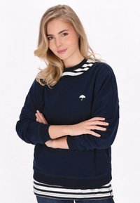 Granatowy sweatshirt z białym logo parasola, paskowany kołnierz, ściągacze przy mankietach i u dołu; nałożony na paskowaną białą i granatową bluzkę.