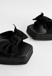 Sorte platform sandaler med en struktureret jutesål, firkantet tå og en overdimensioneret sløjfe lavet af blødt stof. Glat læderoverdel.