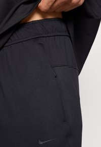 Μαύρο αθλητικό παντελόνι με ελαστική μέση, πλαϊνή τσέπη και λογότυπ ο Nike. Το υλικό είναι λείο με ελαφριά λάμψη.