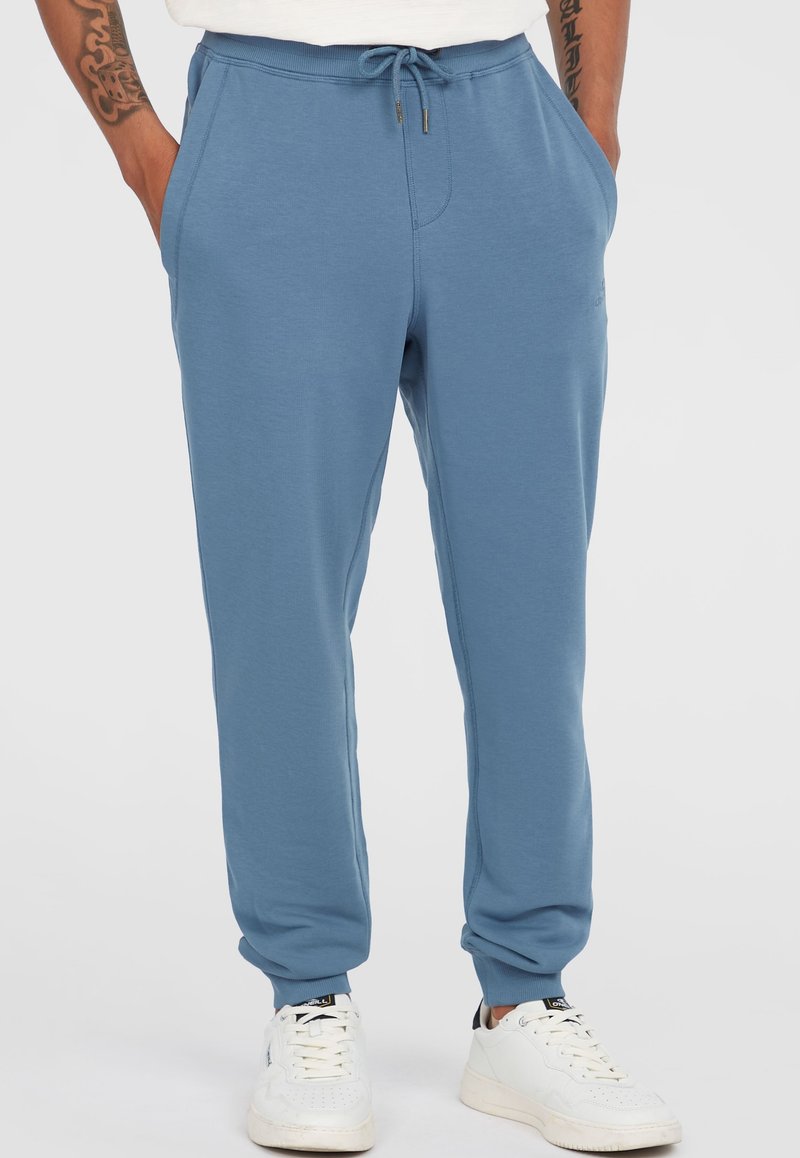 Light blue jogger pants made from soft material, featuring an elastic waistband with a drawstring and side pockets. Accented with ribbed cuffs.