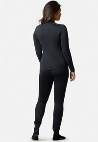 Svart långärmad åtsittande topp och matchande leggings i slät, stretchig tyg. Bakifrån visas en elegant design med minimala sömmar och utan logotyper.