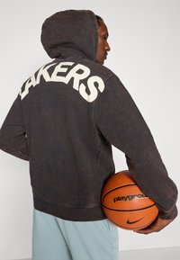 Dark, distressed hoodie with "LAKERS" in large, white letters on the back. The model holds an orange basketball with black accents.