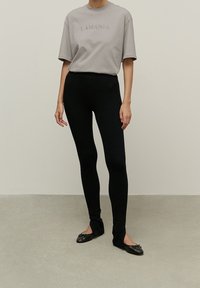 Gray short-sleeve t-shirt with "LAMANIA" embossed text, paired with form-fitting black leggings and black ballet flats with bow accents.