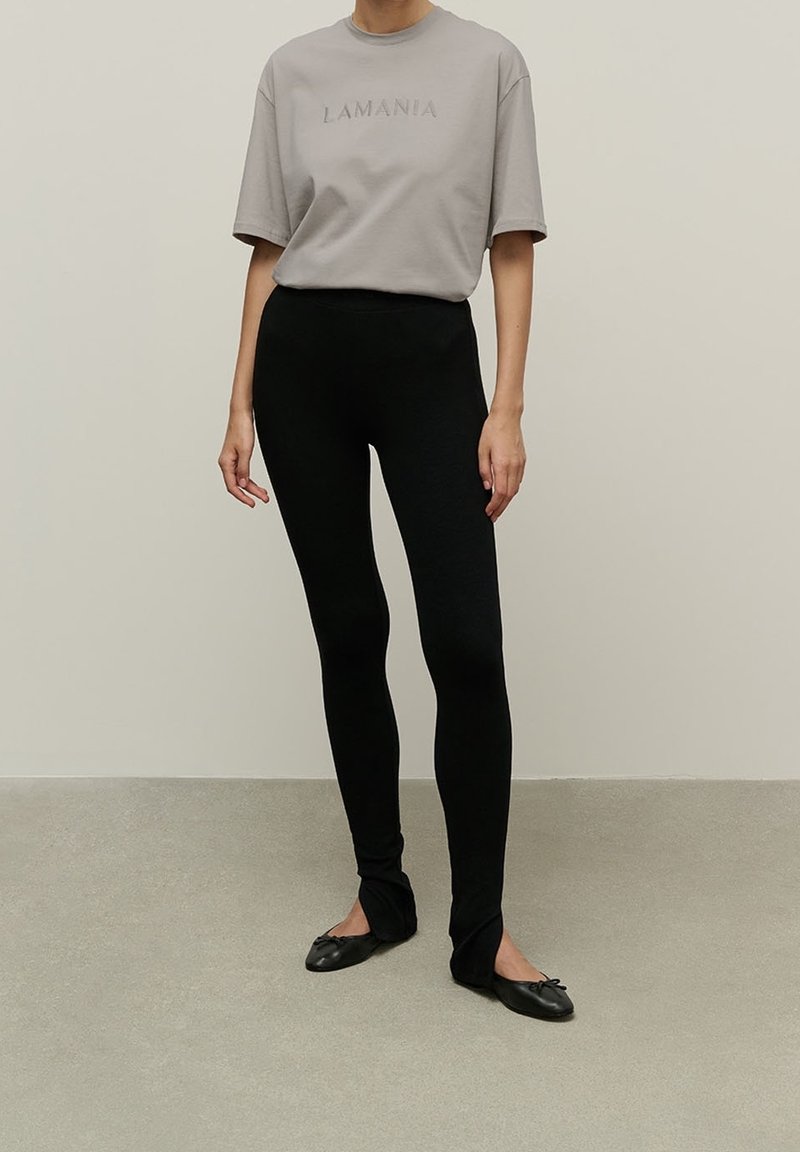 Gray short-sleeve t-shirt with "LAMANIA" embossed text, paired with form-fitting black leggings and black ballet flats with bow accents.