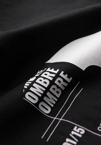 Mustaa kangasta, jossa on toistuva valkoinen lihavoitu teksti "OMBRE", osittain näkyviä geometrisia muotoja ja ohuita valkoisia viivoja kaarevalla pinnalla.