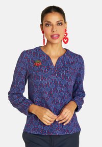 Navy Bluse mit floralem Muster in Rot und Weiß, V-Ausschnitt und langen Ärmeln; verziert mit einem gestickten Kirschdetail.