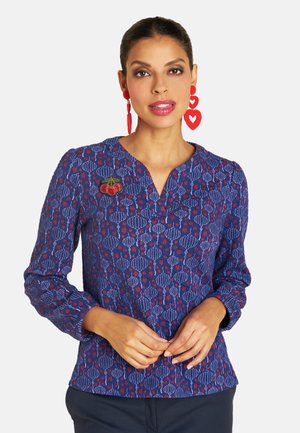 Navy blouse featuring a floral pattern in red and white, v-neck, and long sleeves; accented with an embroidered cherry detail.
