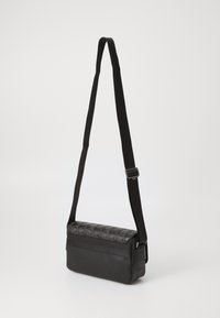 Sort crossbody taske med tekstureret quiltet mønster på toppen, flad form, justerbar strop og glat bundflade.