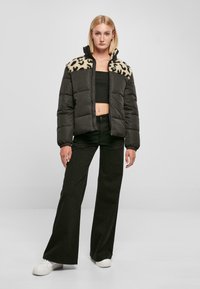 Gevoerde donkergroene jas met een nepbontkraag in luipaardprint, ritssluiting, elastische manchetten en zwarte gedetailleerde broek, gecombineerd met witte sneakers.