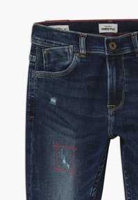 Vaqueros de mezclilla azul oscuro con una zona desgastada y adornos de costura roja, además de un diseño clásico de cinco bolsillos.