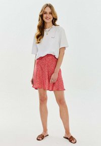 Bílý zkrácený tričko s malým vyšitým detailem, spárované s růžovou sukní s květinovým vzorem, která má rozšířený lem a hladkou texturu.