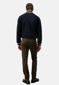 Giacca in pile blu navy con finitura testurizzata, contrastata da bordi a costine; abbinata a pantaloni verde oliva e scarpe nere.