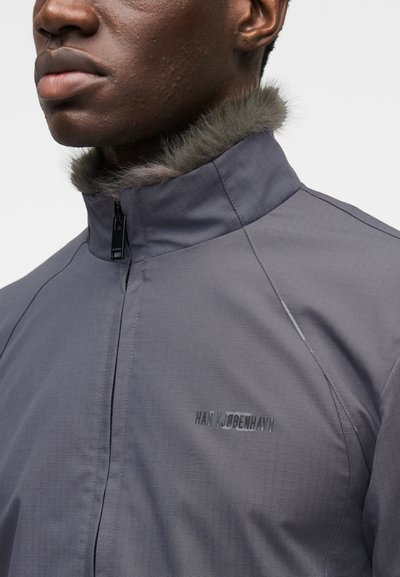 Γκρι ζακέτα με φερμουάρ και επένδυση από γούνα στον γιακά, υφή υφάσματος με ανάγλυφο σχέδιο και διακριτική σήμανση. Διαθέτει ψηλό γιακά και δομημένες ραφές για ένα κομψό, εφαρμοστό ύφος.