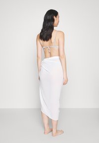 Falda envolvente blanca y transparente, textura suave, diseño drapeado. Tirantes finos en la parte trasera de una blusa de color claro, con herrajes mínimos y un estilo simple.