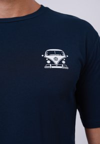 Navy blue t-shirt with a white graphic design of a classic van on the left chest area, featuring a peace sign in the front grille.