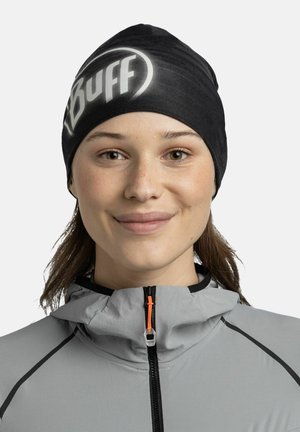 Schwarze Mütze mit einem weißen "Buff"-Logo, aus weichem, elastischem Material. Getragen mit einer hellgrauen Jacke, die eine orangefarbene Reißverschlussdetails aufweist.