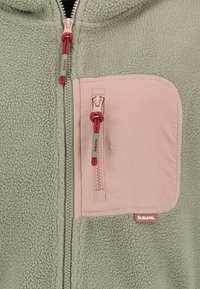 Zielona polarowa kurtka z różową kieszonką na zamek na piersi, czerwoną linką do regulacji i metką marki. Miękka tekstura z przytulnym wzorem.