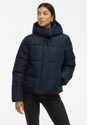 Mörkblå puffjacka med hög krage, kviltad design och stor huva. Mjuk, slät textur och sidofickor. Avslappnad stil.