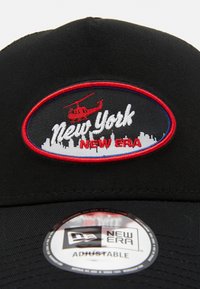 Svart justerbar caps med broderte "New York"-tekst, en rød helikopter, og skyline-design på en sirkulær lapp med røde og blå detaljer.