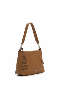 Brązowa skórzana torebka o fakturowanej powierzchni, z regulowanym paskiem i zawieszką w kształcie misia. Widoczna boczna kieszeń.