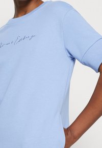 Ljusblå kortärmad sweatshirt i mjuk bomull med ribbad mudd, med broderad text "Armani Exchange" på framsidan.