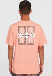 Lyse orange bomulds t-shirt med grafisk design med sol- og månemotiver, kantet af intrikate mønstre på ryggen.