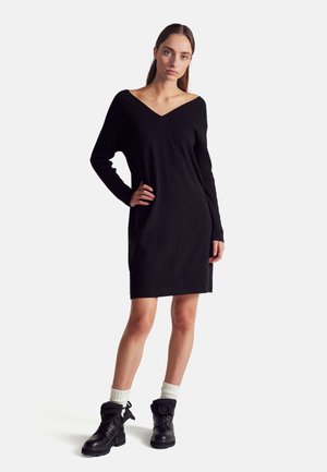 Vestido negro de punto con escote en V, mangas largas y textura acanalada. Llevado con botas negras hasta el tobillo y calcetines grises hasta la rodilla.