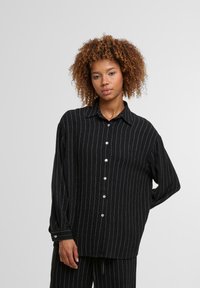 Black striped button-up shirt with long sleeves and a loose fit. Features white vertical stripes and a classic collar with buttons down the front.