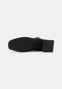 Suela de zapato negra con un tacón cuadrado, que presenta una superficie de goma texturizada y una plantilla suave y ligeramente curvada para mayor estabilidad.