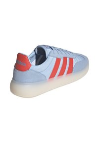 Plave suede i mrežaste tenisice s crvenim prugama, podstavljenim ovratnikom i prozirnom gumenom potplatom. Ovratnik i 'adidas' brendiranje su vidljivi.