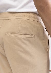 Pantalon beige en tissu léger, doté d'une taille élastique et d'une poche arrière avec une texture lisse.