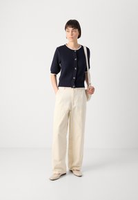 Navy knitted cardigan with short sleeves, button front, white accents. Paired with pale beige wide-leg pants and neutral slip-on shoes.