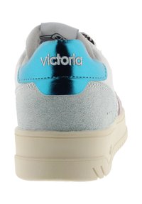 Vit sneaker med en blå metallisk hälflik, texturerade ljusblå mockadetaljer och en beige gummisula. "Victoria"-logotypen är sydd i vitt.