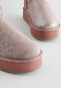 Bottines à plateforme en rose gold scintillant avec une texture lisse, dotées d'une semelle rose solide et d'un design à bout rond.