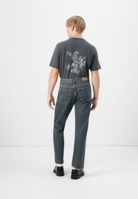 Gray t-shirt featuring a decorative print on the back, paired with dark blue jeans. The outfit includes black shoes and a visible label on the jeans.