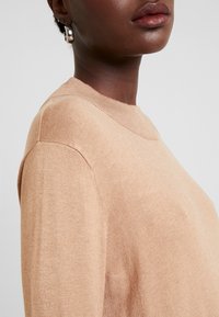 Maglione beige chiaro con scollatura tonda, texture morbida e dettagli a coste ai bordi, mostrato di lato.