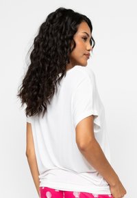 T-shirt bianco a maniche corte realizzato in tessuto morbido, vestibilità ampia con scollatura rotonda; indossato con pantaloni rosa con motivi di conchiglie bianche.