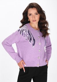 Cárdigan de punto lila con botones de perlas y diseño de alas con lentejuelas en el hombro izquierdo, que presenta una textura suave y un corte holgado.