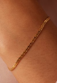 Gold chain bracelet on a wrist, featuring interlocking oval links with a smooth, polished texture. Simple, delicate design.