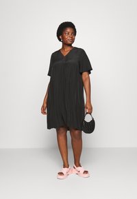 Vestido preto à altura dos joelhos com decote em V e mangas curtas, combinado com sandálias plataforma rosas e uma bolsa preta. Textura suave.