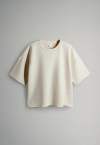 Beige īsām piedurknēm T-krekls, izgatavots no mīksta auduma, ar apaļu kakla izgriezumu un vaļīgu piegriezumu ar taisnu apakšmalu. Nav redzamu rakstu vai akcentu.