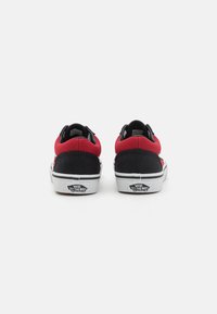 Red and black canvas sneakers with a low-top design, white rubber soles, and Vans branding on the heel. Simple stitching detail.