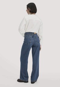 Witte blouse met lange mouwen in een relaxte pasvorm, gecombineerd met high-waisted blauwe denim jeans met rechte pijpen en twee achterzakken.
