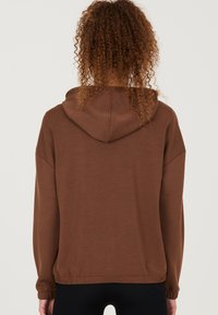 Un sweat à capuche marron avec un cordon de serrage, des manches longues et des poignets élastiques. Texture lisse et coupe décontractée, avec un ourlet froncé.