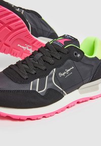 Sneakers neri con tomaia texturizzata, suola in gomma rosa, dettagli neon verdi e logo argentato. Presentano un sistema di allacciatura tradizionale.