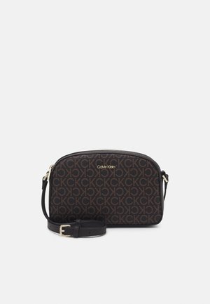 Sac crossbody noir Calvin Klein avec motif répétitif du logo CK marron et bandoulière amovible et ajustable sur fond blanc.