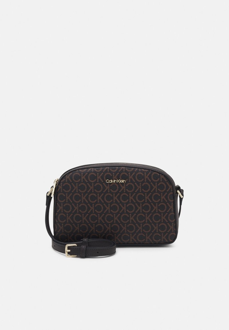 Schwarze Crossbody-Tasche von Calvin Klein mit braunem, wiederholtem CK-Logo-Muster und abnehmbarem, verstellbarem Tragegurt auf einem weißen Hintergrund.