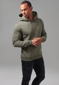 Olijfgroene hoodie gemaakt van een zachte katoenen mix, met een voorkantzak, koordjes en ribboorden aan de mouwen en onderkant.